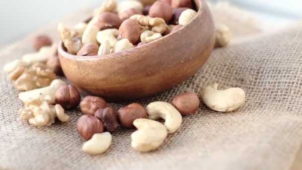 Mixed nuts in a wooden cup against the background of fabric from burlap. Walnut, hazelnuts and cashews. Wood bowl with different tasty nuts — Stock Video