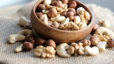 Çuval bezi kumaşının arka planına karşı ahşap bir fındıkta karışık fındık. Ceviz, fındık ve fındık. Farklı fındıklı ahşap kase.