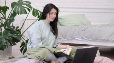 Genç kız yerde ödev yapıyor. Genç kız öğrenci notlar yazıyor internetten video izleyip bilgisayardan öğreniyor. uzaklık öğrenme kursu video konferans pc çağrısı.