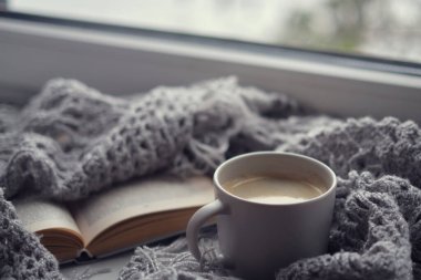 Bir fincan kahve ve bir kitapla rahat bir ev. Hygge tarzı. Tahta tahtada sıcak atkı ile sarılmış siyah kahve bardağı. Üst görünüm, vintage tarzı, Natürmort.