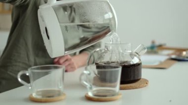 Kadın elektrikli çaydanlıktan çaydanlığa sıcak su dolduruyor..