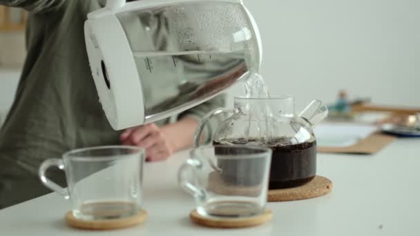 Vrouw giet warm water uit een waterkoker in een theepot met losse thee. — Stockvideo