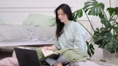 Genç kız yerde ödev yapıyor. Genç kız öğrenci notlar yazıyor internetten video izleyip bilgisayardan öğreniyor. uzaklık öğrenme kursu video konferans pc çağrısı.