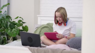 Pembe saçlı genç kız internetten resim yapmayı öğreniyor. Yatak odasında yatakta oturmuş ödev yapan tatlı bir kız.