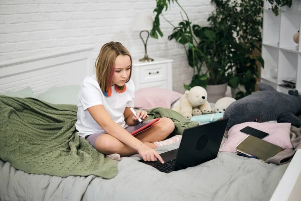 Tinédzser lány házi feladatot csinál az ágyon. tini lány iskolás diák írni jegyzetek videó online webinar tanulni laptop. távoktatási kurzus videokonferencia pc call. — Stock Fotó