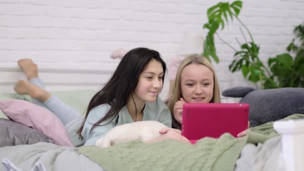 Duas meninas adolescentes sentam-se no laptop e olham para o monitor conversando com amigos através de vídeo chat. — Vídeo de Stock