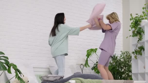 Mladé dívky tančí doma na posteli. Dvě mladé nadnárodní dívky tráví spolu čas na pyžamové párty. nejlepší přítelkyně se selfie. — Stock video