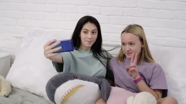 Zwei junge multinationale Mädchen verbringen Zeit miteinander, Pyjama-Party. Beste Freundinnen machen Selfies. — Stockvideo