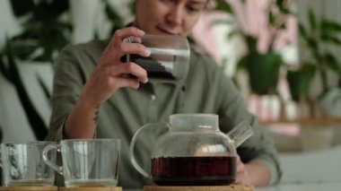 Keten gömlekli kadın iki şeffaf fincana çay döküyor. Konukseverlik konsepti, ev sahibesi misafirlere çay ikram eder.