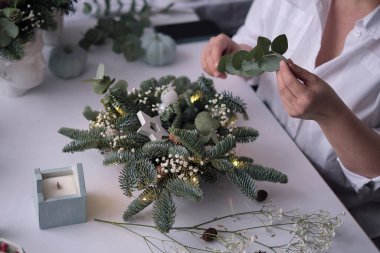 Kadın bir Noel masa süslemesi dekore etmiş. Eller yakın çekim. Dekoratif süsler konusunda yüksek lisans. Noel dekorunu kendi elleriyle yaptılar. Çiçekçi. Köknar dallarının Noel kompozisyonu.