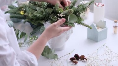 Kadın bir Noel masa süslemesi dekore etmiş. Eller yakın çekim. Dekoratif süsler konusunda yüksek lisans. Noel dekorunu kendi elleriyle yaptılar. Çiçekçi. Köknar dallarının Noel kompozisyonu.