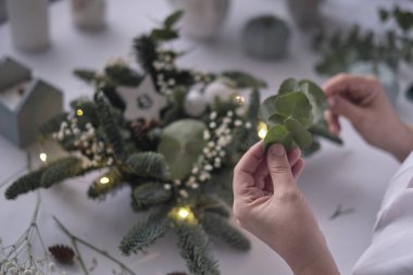 Kadın bir Noel masa süslemesi dekore etmiş. Eller yakın çekim. Dekoratif süsler konusunda yüksek lisans. Noel dekorunu kendi elleriyle yaptılar. Çiçekçi. Köknar dallarının Noel kompozisyonu.