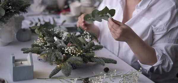 Kadın bir Noel masa süslemesi dekore etmiş. Eller yakın çekim. Dekoratif süsler konusunda yüksek lisans. Noel dekorunu kendi elleriyle yaptılar. Çiçekçi. Köknar dallarının Noel kompozisyonu.
