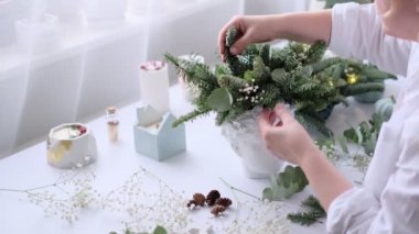 Kadın bir Noel masa süslemesi dekore etmiş. Eller yakın çekim. Dekoratif süsler konusunda yüksek lisans. Noel dekorunu kendi elleriyle yaptılar. Çiçekçi. Köknar dallarının Noel kompozisyonu.