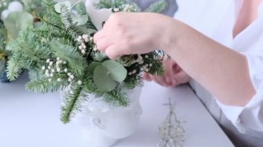 Kadın bir Noel masa süslemesi dekore etmiş. Eller yakın çekim. Dekoratif süsler konusunda yüksek lisans. Noel dekorunu kendi elleriyle yaptılar. Çiçekçi. Köknar dallarının Noel kompozisyonu.