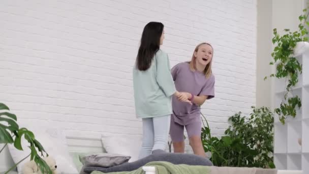 Jeunes filles dansant sur le lit à la maison. Deux jeunes multinationales passent du temps ensemble, en pyjama. meilleures copines prennent selfies. — Video