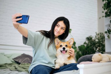 Genç kız evde köpeğiyle selfie çekiyor. Evcil hayvanlı köpek sever. Modern teknoloji, insanlar ve hayvanlar konsepti