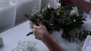 Kadın bir Noel masa süslemesi dekore etmiş. Eller yakın çekim. Dekoratif süsler konusunda yüksek lisans. Noel dekorunu kendi elleriyle yaptılar. Çiçekçi. Köknar dallarının Noel kompozisyonu.