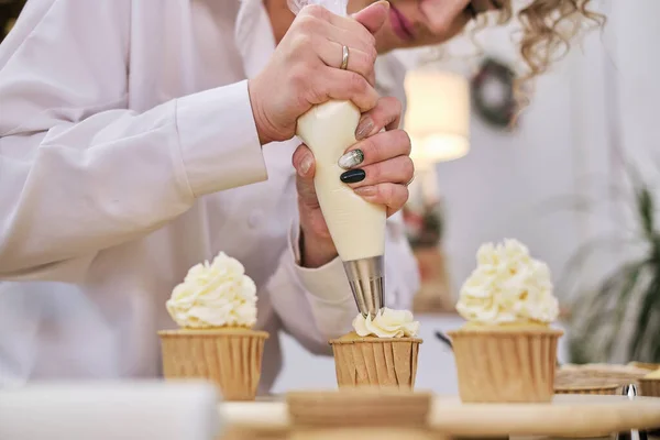 Confeiteiro espreme um creme branco na forma de flores de rosas. processo de decorar cupcakes com chantilly branco. Decorar um bolo branco com creme do saco de pastelaria. — Fotografia de Stock