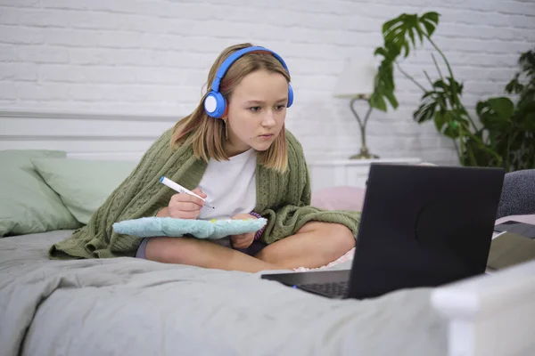 Adolescente haciendo deberes en la cama. adolescente estudiante de la escuela escribir notas ver video webinar en línea aprender en el ordenador portátil. curso de aprendizaje a distancia video conferencia pc llamada. —  Fotos de Stock