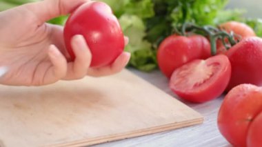 Mutfak bıçağını kullanarak ahşap kesim tahtasıyla taze domates, domates filizi ve arka planda marul kesiyor.