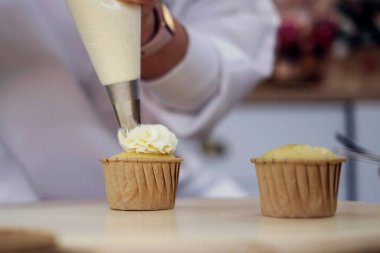 Şekerci gül çiçeği şeklinde beyaz bir krema sıkıyor. Kekleri beyaz kremayla dekore etme süreci. Pasta poşetindeki kremayla beyaz bir pasta süslüyorsun..