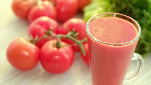Tomatjuice med kvist tomater på bakgrunden. Tomatjuice hälls i ett glas. — Stockvideo