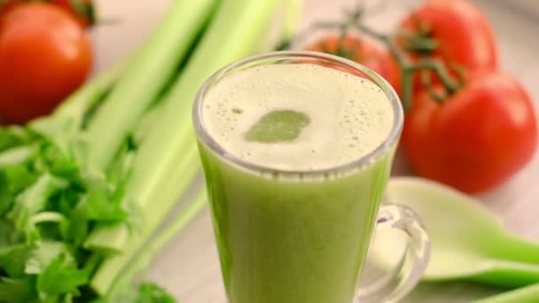 Slow motion drops of celery smoothies dripping into a glass of juice, with sprig of tomatoes on background. celery juice is poured into a glass. — Vídeo de stock