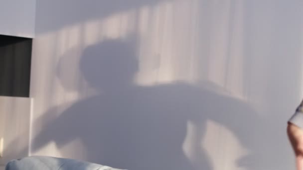 Little smiling boy playing with shadows on the wall. shadow of a dancing boy reflected on the wall, carefree childhood — Stockvideo