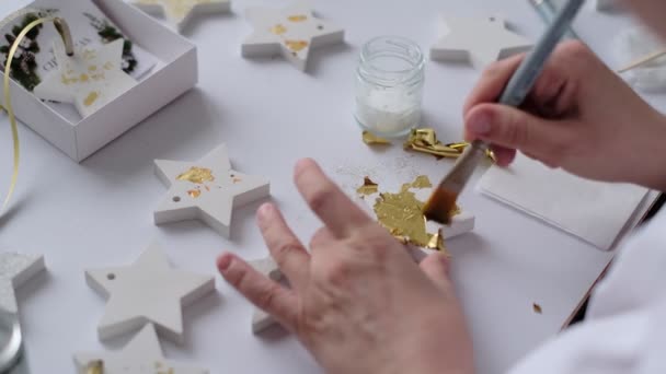 Påfører gylne blader. kvinnelig kunstner dekorerer gullpussen med et gullark. – stockvideo