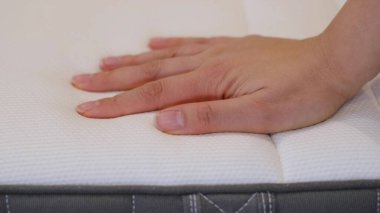 Kadın iyi bir uyku için yeni bir yatak seçiyor. Kadının eli yatak kalitesini test ediyor. Yumuşaklığı kontrol ediyorum. En iyi tip ve kalitede bir seçim. Yan görüş. Yakın çekim..