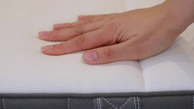 Kadın iyi bir uyku için yeni bir yatak seçiyor. Kadının eli yatak kalitesini test ediyor. Yumuşaklığı kontrol ediyorum. En iyi tip ve kalitede bir seçim. Yan görüş. Yakın çekim..