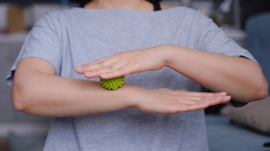 Genç bir kadın, yeşil bir miyofasyal topla kol kaslarını çalıştırıyor. Lastik topla egzersiz yapan bir kadın.
