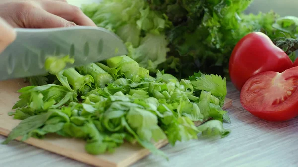 Woman hands using a knife to slice a bunch of fresh celery. Food fresh stalks of Celery peeling. Culinary delicious food being prepared. Stock Picture