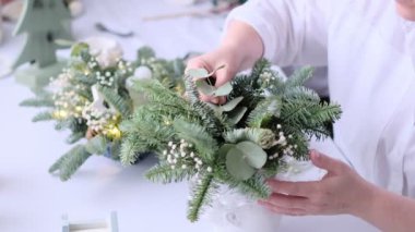 Kadın bir Noel masa süslemesi dekore etmiş. Eller yakın çekim. Dekoratif süsler konusunda yüksek lisans. Noel dekorunu kendi elleriyle yaptılar. Çiçekçi. Köknar dallarının Noel kompozisyonu.