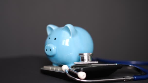 Банк свиней со стетоскопом и калькулятором на черном фоне, концепция медицинского страхования — стоковое видео