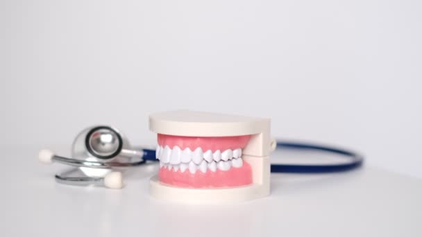 Λευκό μοντέλο δοντιών και στηθοσκόπιο σε λευκό φόντο. φροντίδα δοντιών. έννοια της προληπτικής εξέτασης της στοματικής κοιλότητας. — Αρχείο Βίντεο