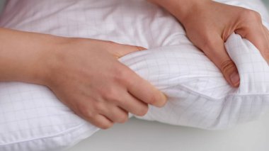 Genç bir kadın yumuşak beyaz yastığa dokunuyor, yakın plan. Yastık nasıl seçilir, yapay dolgu.