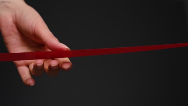 Mano con tijeras cortando el concepto de ceremonia de apertura de cinta roja. sobre fondo negro — Vídeos de Stock