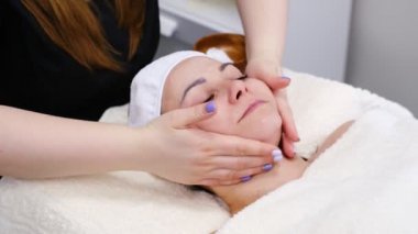 Kadın güzellik salonunda yüz masajı yaptırıyor. Sağlıklı yaşam tarzı ve vücut bakımı kavramı. Yavaş çekim, yakın çekim.