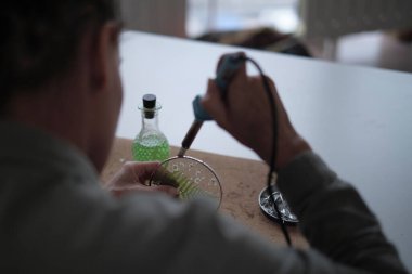 Lekeli cam imalatçısı renkli hatıralarla çalışır. Kadın elleri lehimlenmiş camları lehimliyor, vitray yapmayı öğreniyor, el işi bitiriyor, silah lehimliyor.