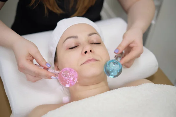 Calm patient woman undergoing the cosmetic facial massage procedures for rejuvenation skin face and doctor using cosmetic instruments, ice balls massage. Stock Image