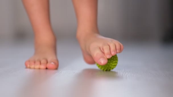 Un niño pequeño masajeando con una pelota en el pie. El ejercicio estimula el desarrollo correcto del pie. Ejercicio de corrección pies planos. Primer plano del vídeo. Movimiento lento — Vídeo de stock