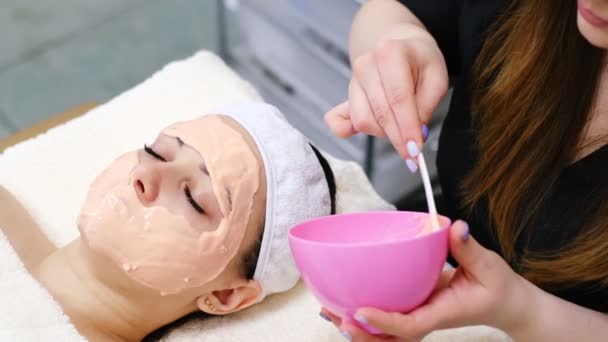 Gezichtsbehandeling. Jonge vrouw ontvangt kosmetisch masker in schoonheidssalon. Beautician Alginate Mask aanbrengen op vrouwelijk gezicht met gladde zachte huid. Cosmetologie. — Stockvideo