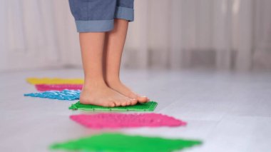 Küçük çocuk farklı doku ve sertlikte ortopedik masaj minderlerine basıyor. Tetik Noktalı Dikenli Masaj Topuyla Ayak Masajı. Miyofasyal Salıverme. Kapat..