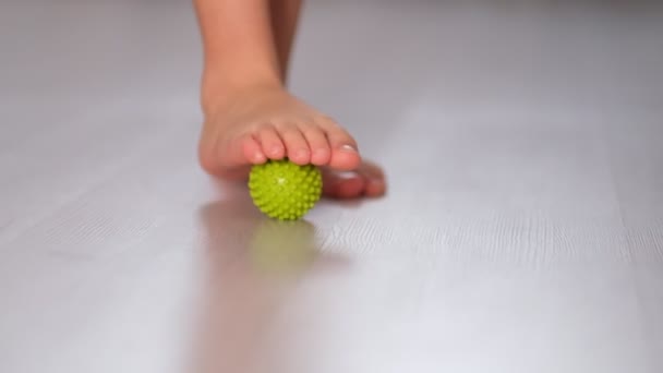 Un niño pequeño masajeando con una pelota en el pie. Masaje de pies con punta de gatillo Spiky Massage Ball. Liberación miofascial. De cerca. Vídeo filmado. Movimiento lento — Vídeos de Stock