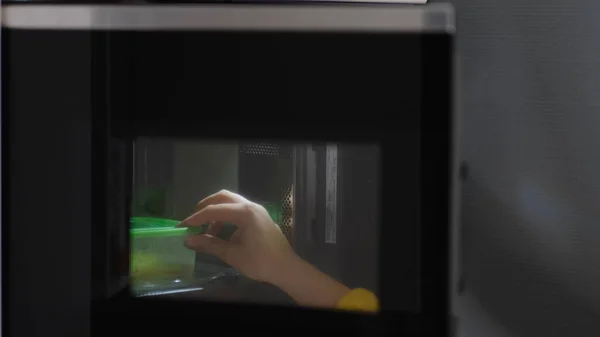 Mujer manos calentando un recipiente de comida en el horno de microondas moderno para el almuerzo de aperitivos en casa — Foto de Stock