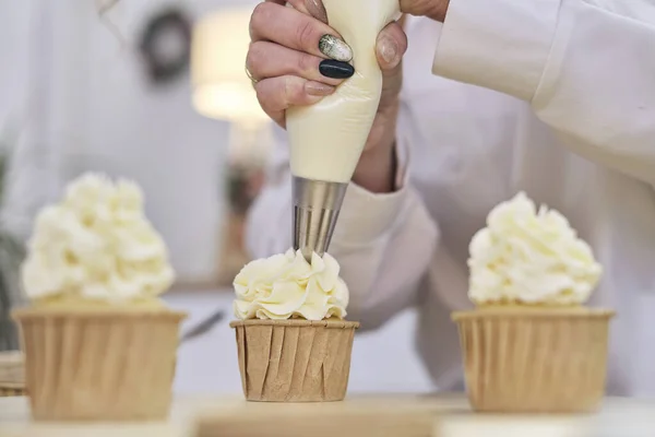 Confeiteiro espreme um creme branco na forma de flores de rosas. processo de decorar cupcakes com chantilly branco. Decorar um bolo branco com creme do saco de pastelaria. — Fotografia de Stock