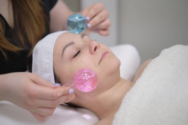 Kozmetik aletler, buz topları masajı ve estetik aletler kullanarak cilt ve doktor yenileme için estetik yüz masajı yapılan sakin bir kadın..
