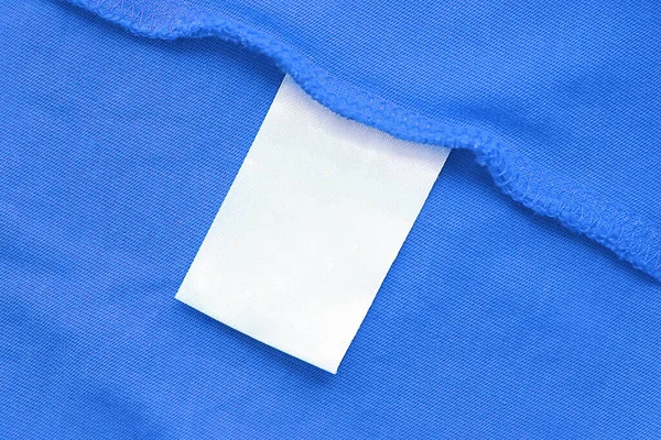 Etiqueta de ropa blanca en blanco para el cuidado de la ropa en tela azul textura fondo. — Foto de Stock